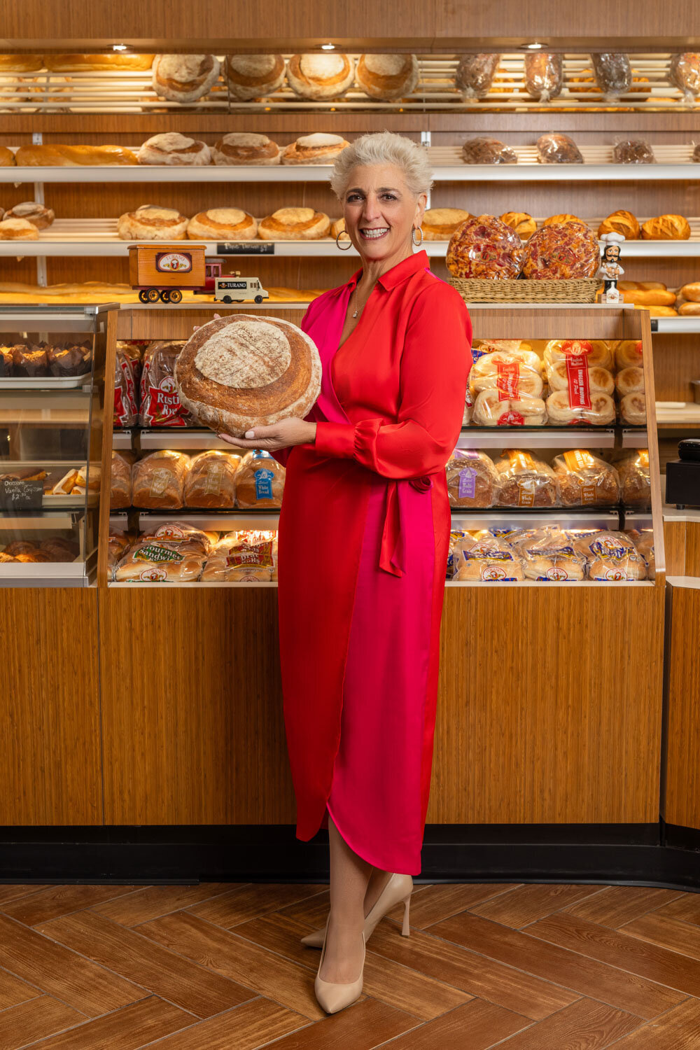 A woman in a red dress is holding a loaf of bread in a bakery.