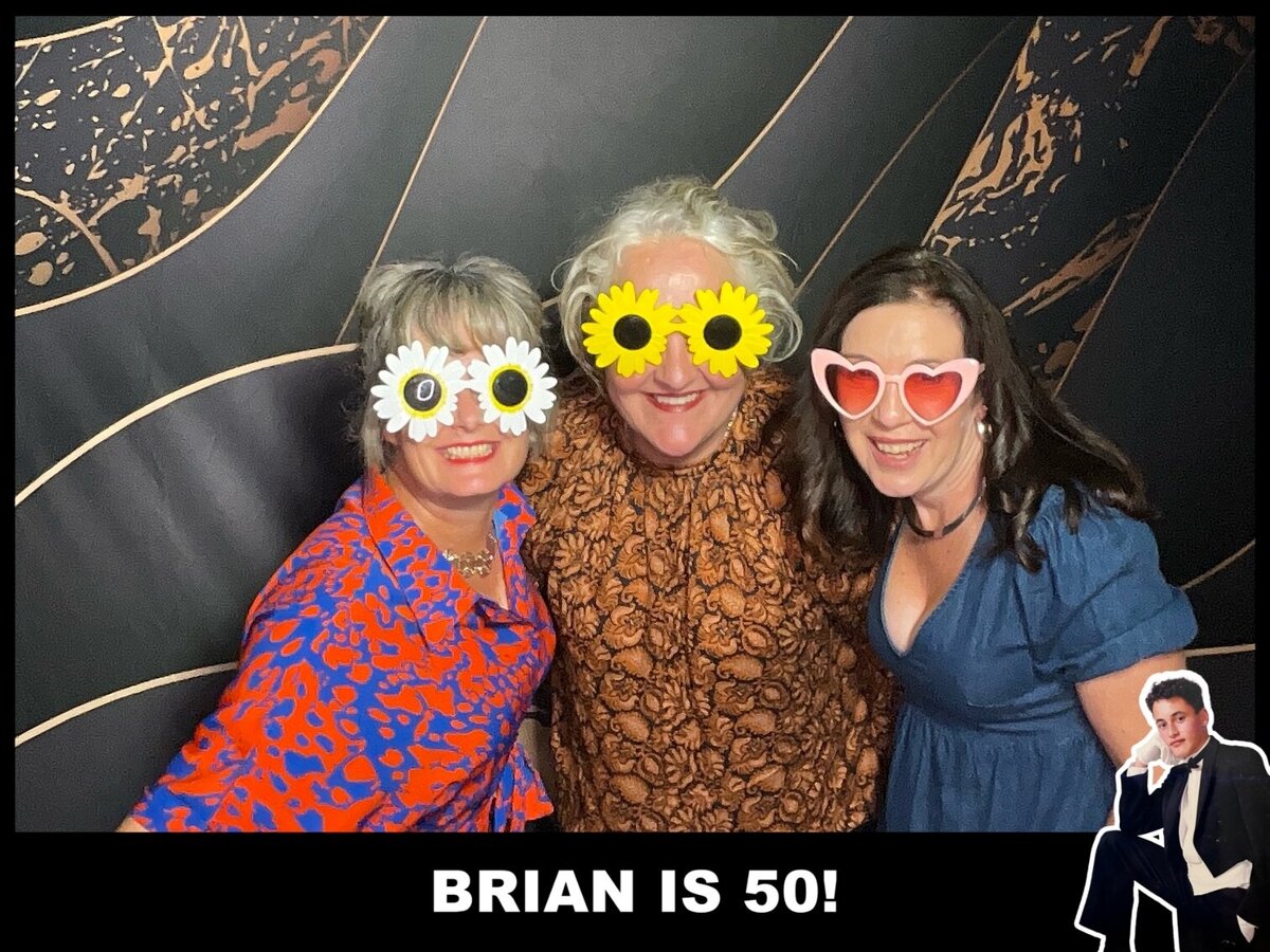 three women pose in front of a black and gold backdrop in a  photo booth at a 50th birthday in christchurch