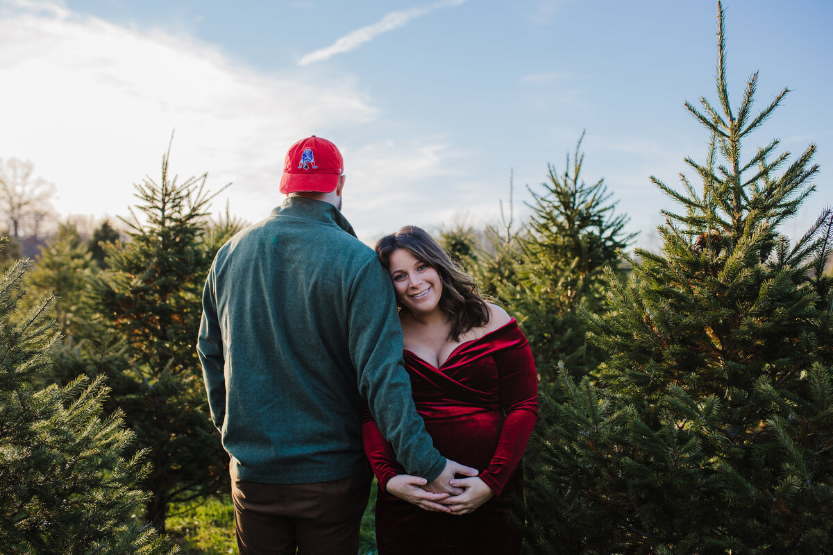maternity in burgundy dress with boyfriend  at a christmas tree farm
