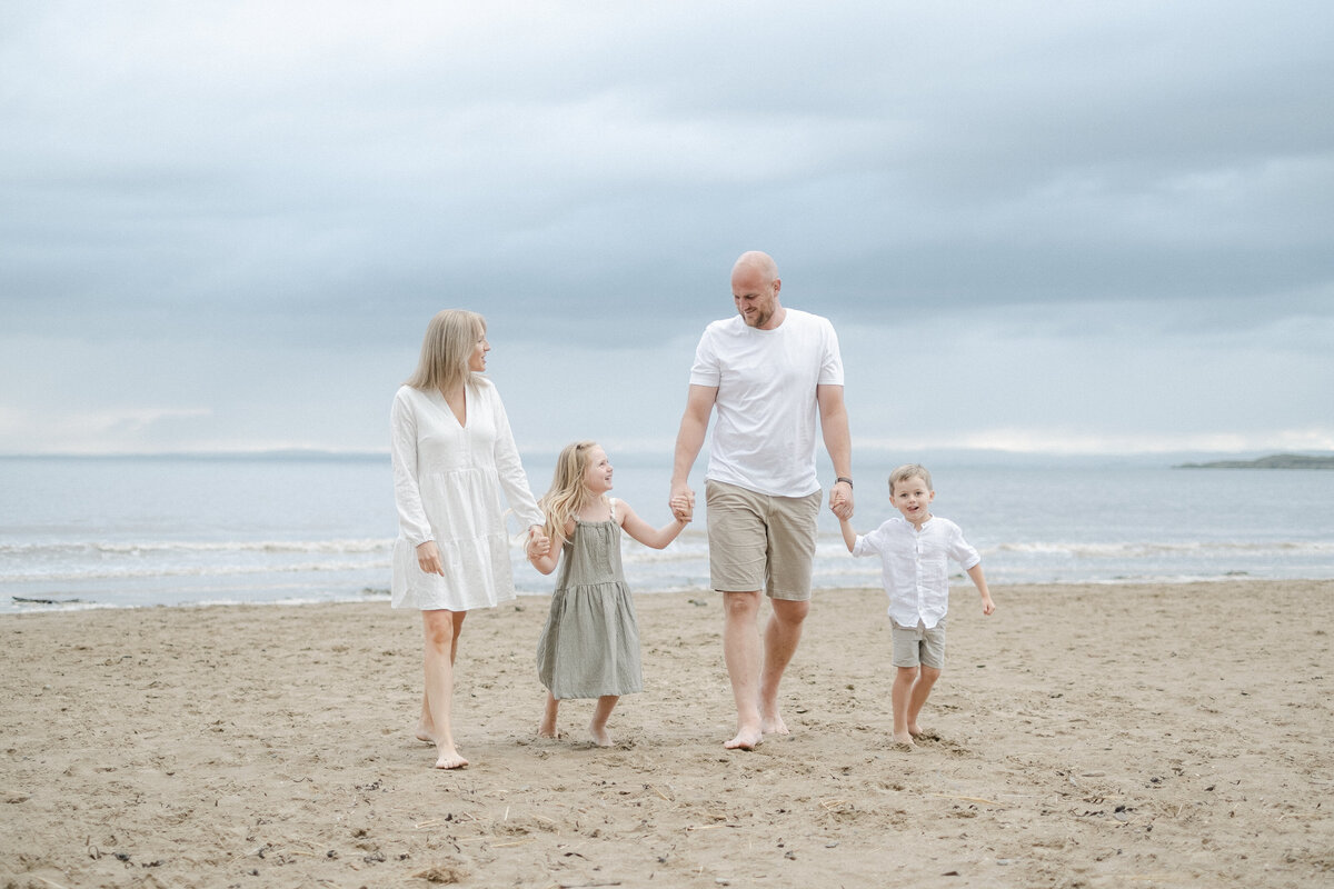 Family walk hand in hand during an outdoor family photoshoot on the beach