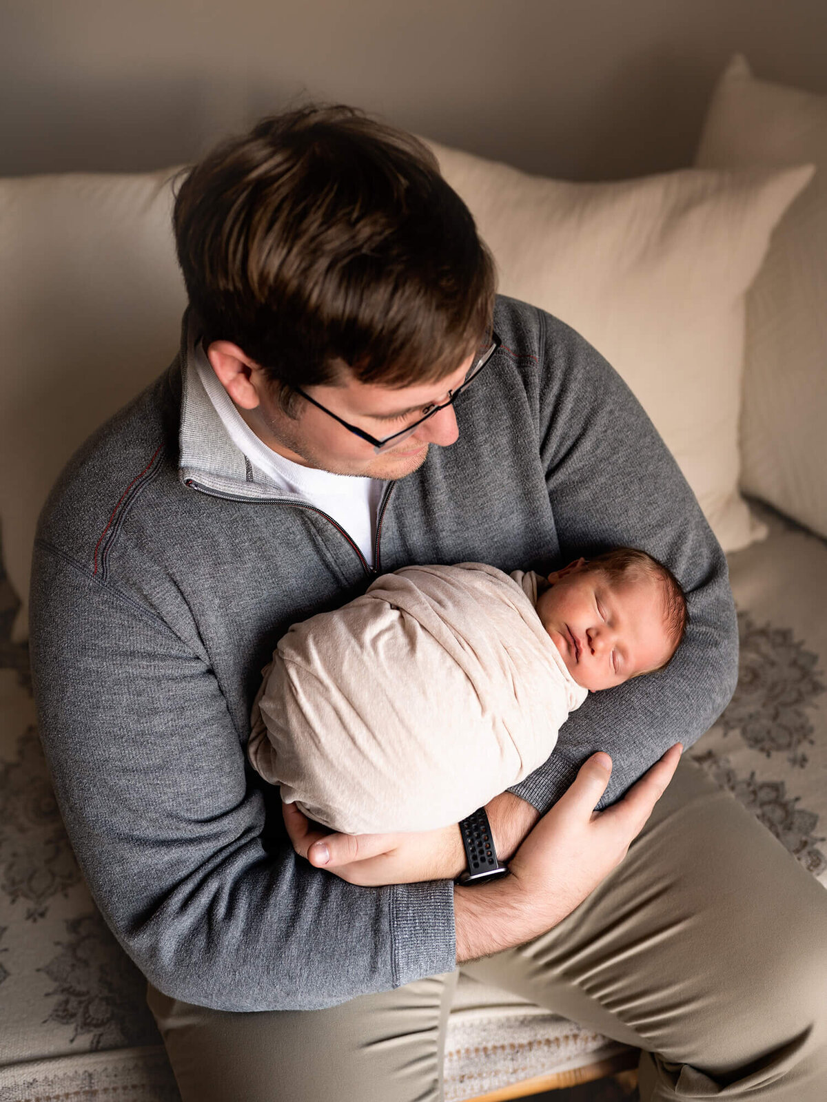 A new dad holds his newborn baby boy who is wrapped in a white blanket and sleeping peacefully