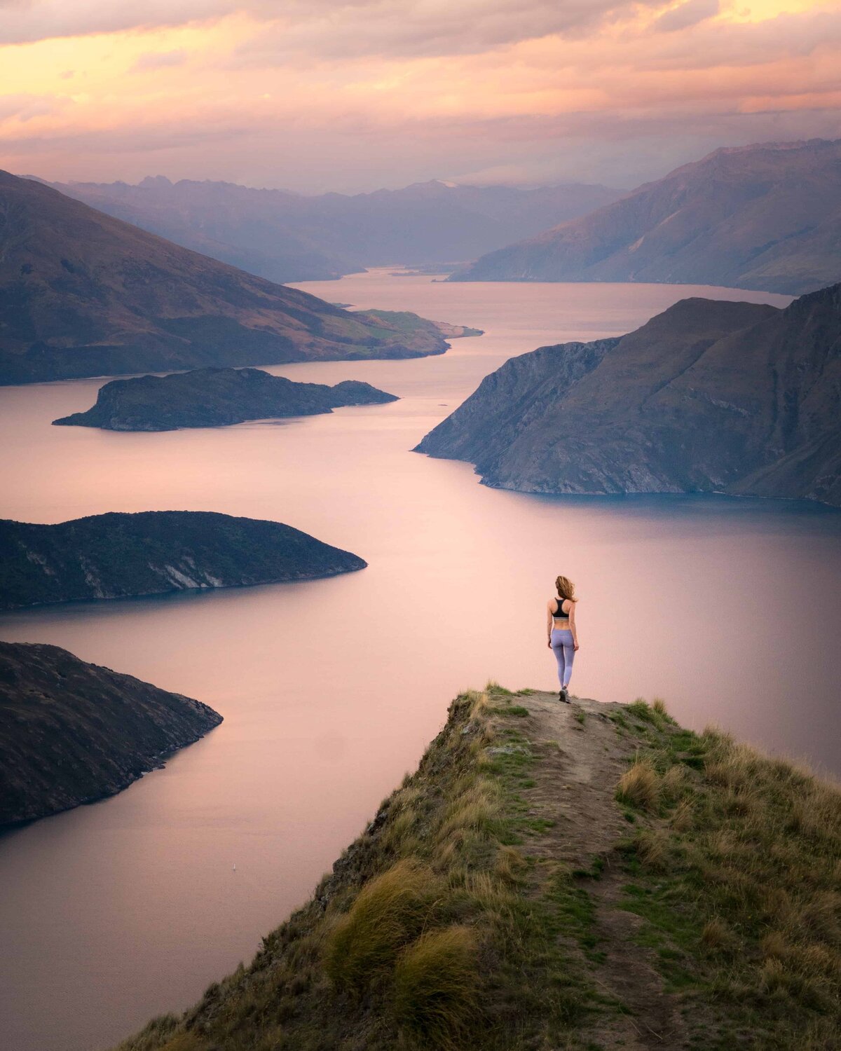 Woman standing on a peak looking down at water and mountains below