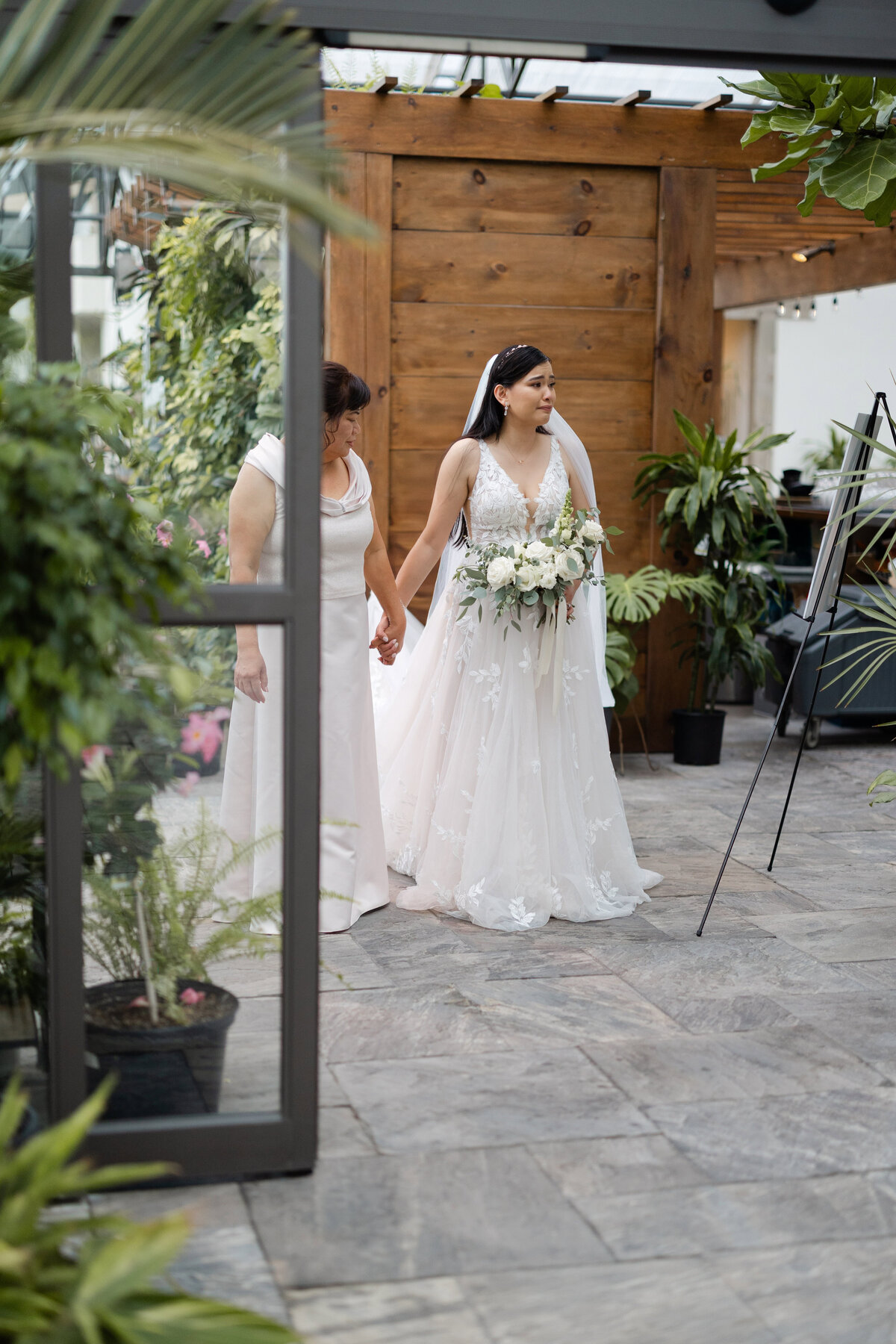 The bride holding her mother's hand as she looks emotionally towards the wedding ceremony