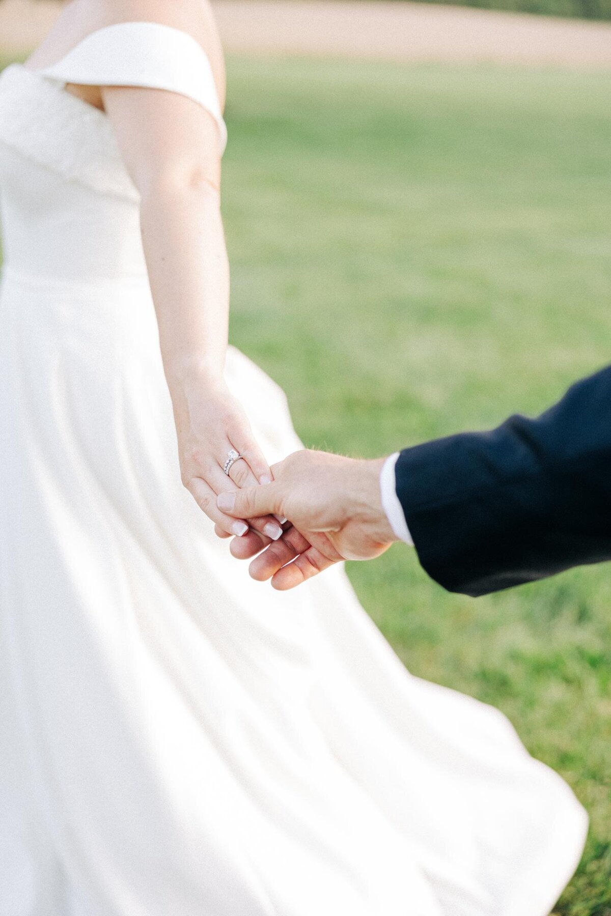 A bride and groom holding hands, with a focus on their intertwined fingers.