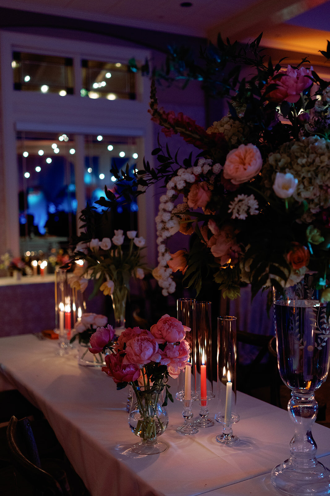 Romantic wedding reception table adorned with vibrant floral centerpieces, including pink roses and cascading greenery, surrounded by glowing candlelight at Burritt on the Mountain.