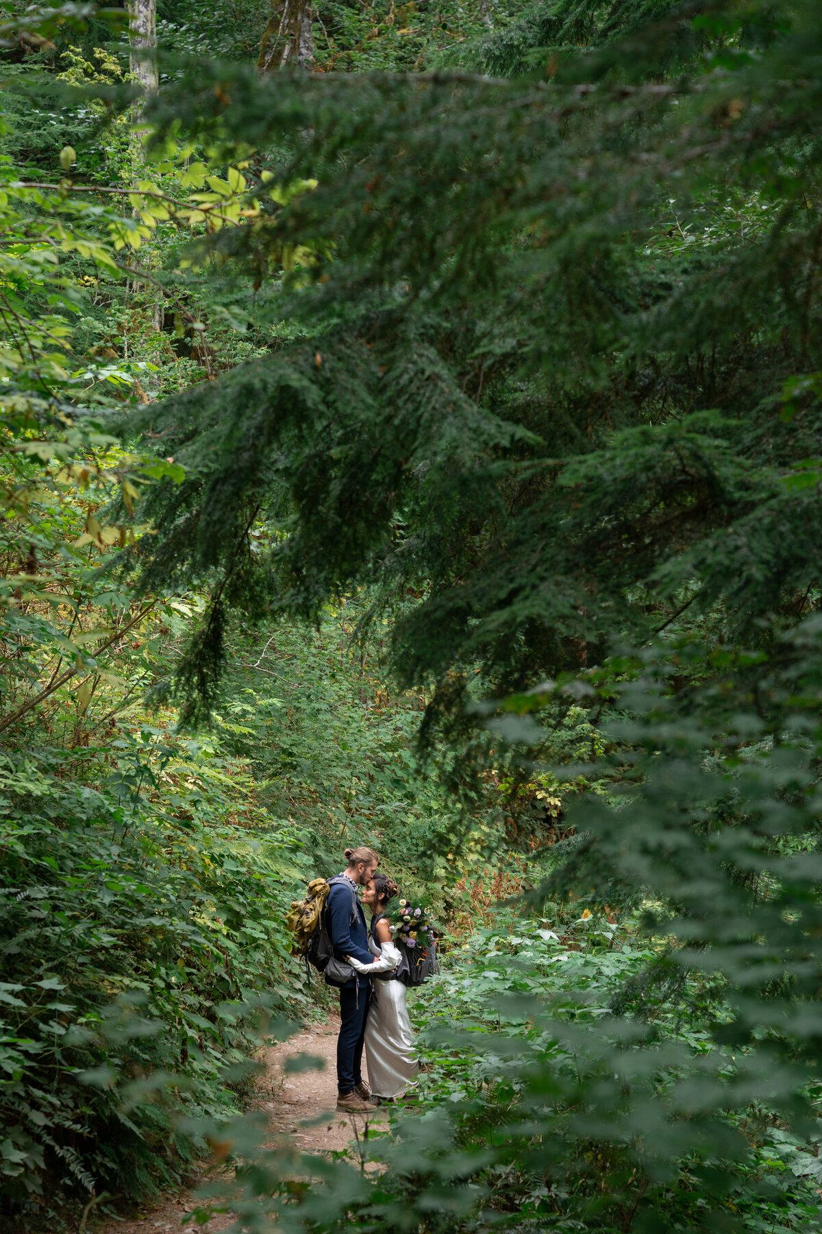 A person kissing their partner's head as they hike in the forest