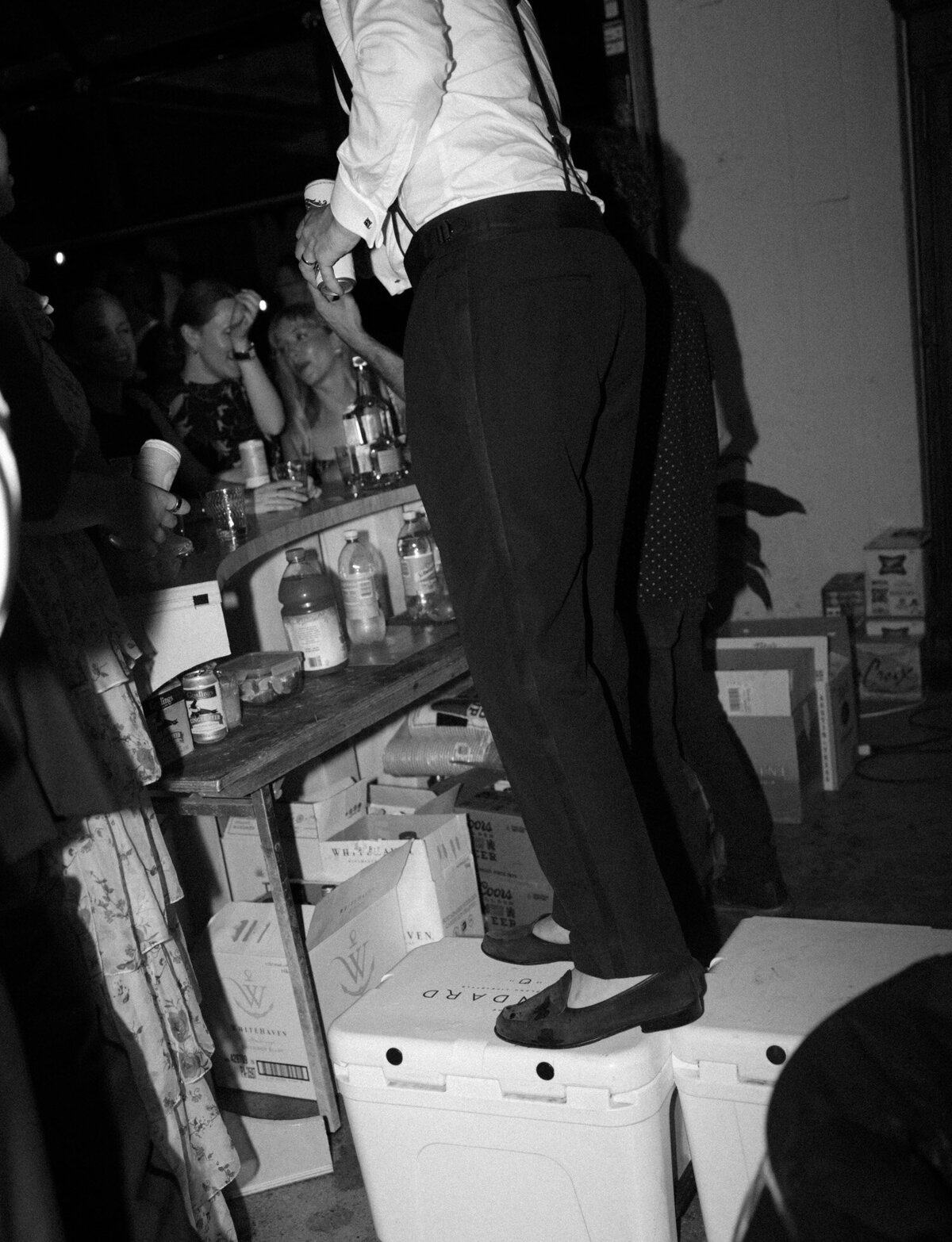 groom stands on a cooler to bartend during his wedding afterparty in Detroit