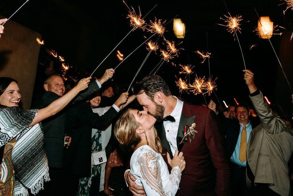 Bride and groom share a kiss under sparklers with their guests.