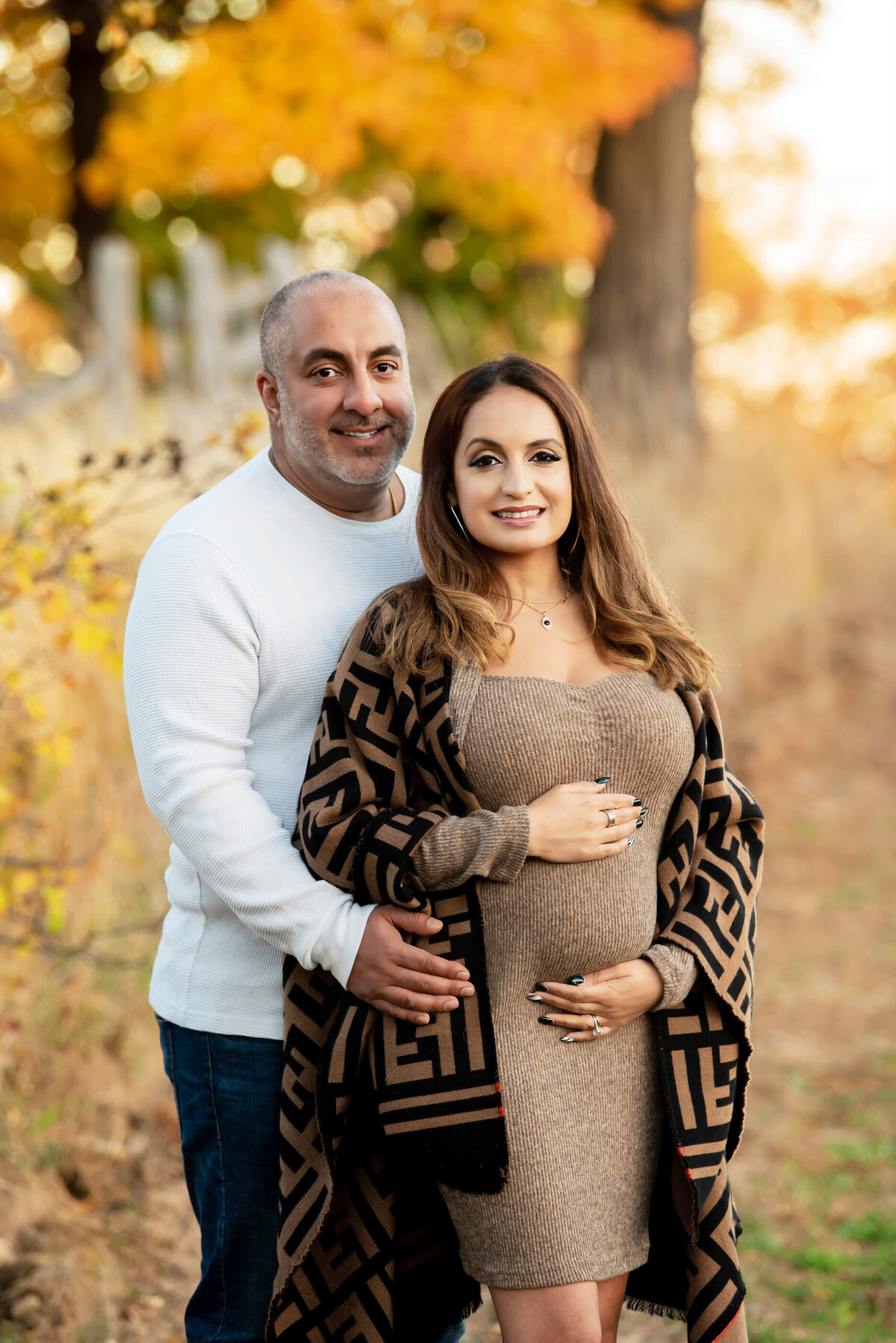 husband standing behind wife with their hands on her belly for their outdoor fall maternity photos in Burlington, ON 