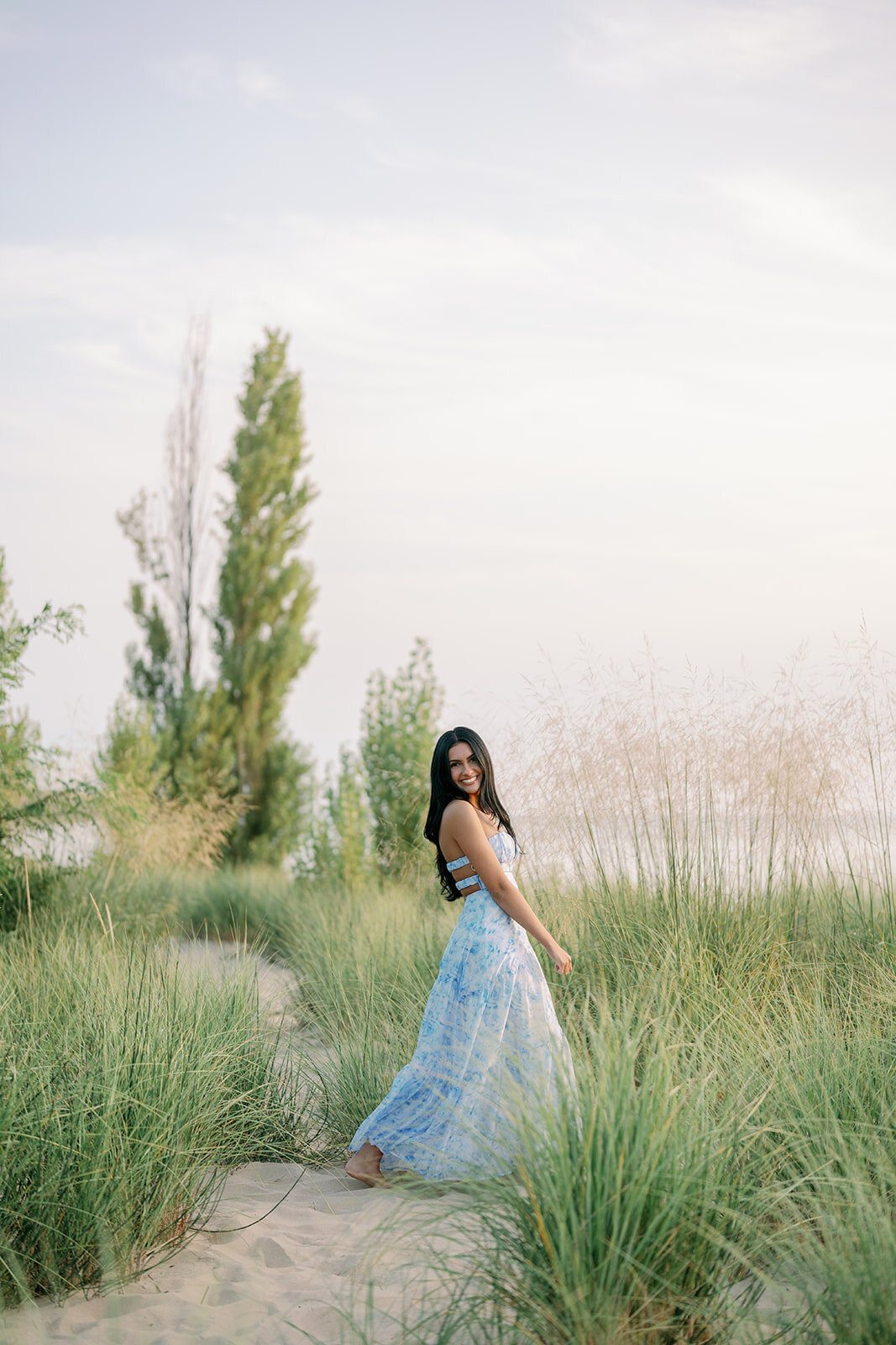 High school senior walking through tall dune grass with Lake Michigan scenery in the background.