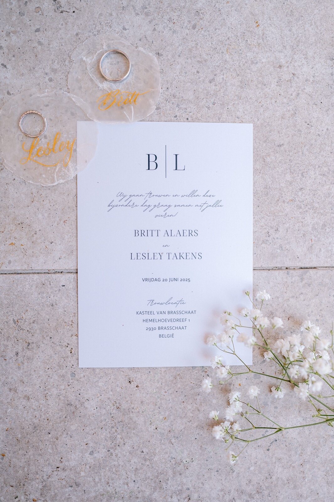 Flatlay van de trouwuitnodiging met ringen en bloemetjes erbij