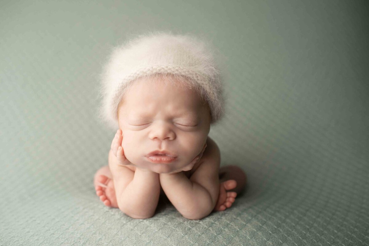 Redhead newborn boy in a cozy, posed position with a peaceful expression, hands near his face