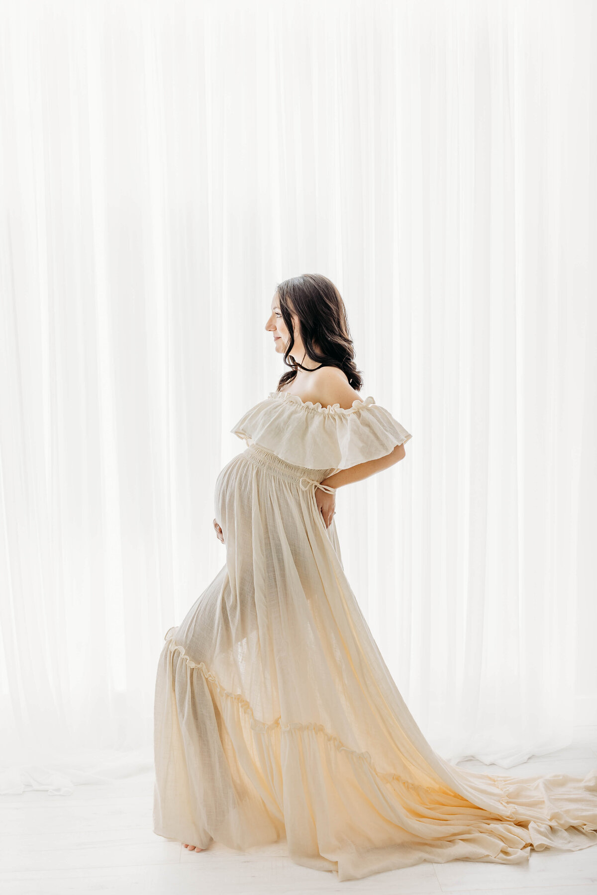 Pregnant mother posing in studio in from of wall of light beautiful dress