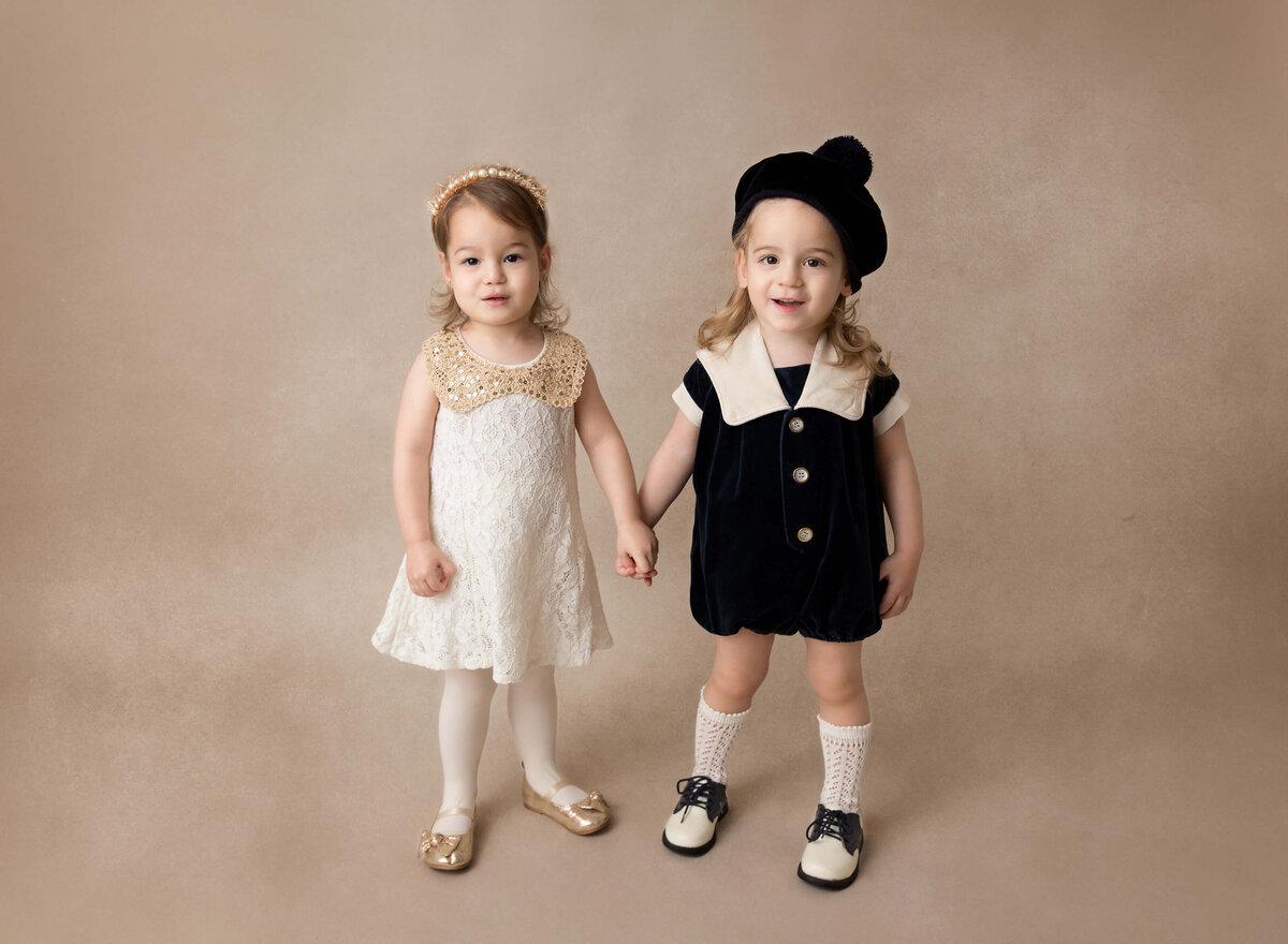Toddler siblings are standing holding hands and smiling at the camera for the upshernesh pictures in NYC