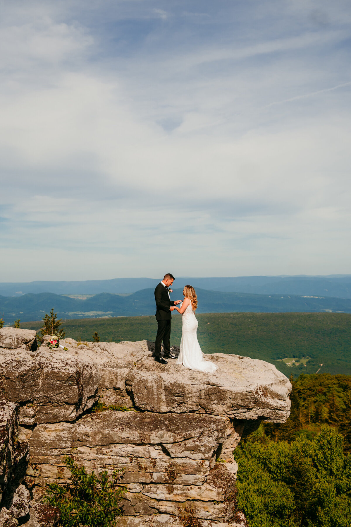 Bride and groom standing on dramatic cliff with panoramic view