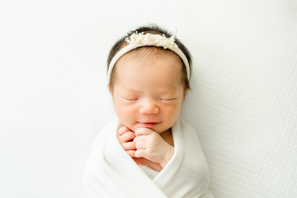 a newborn baby lays on top of a white surface while asleep and smiles while captured by an Austin baby photographer.