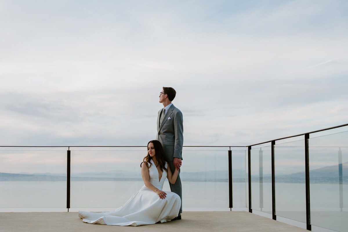 Bride sitting at groom’s feet on modern terrace overlooking water