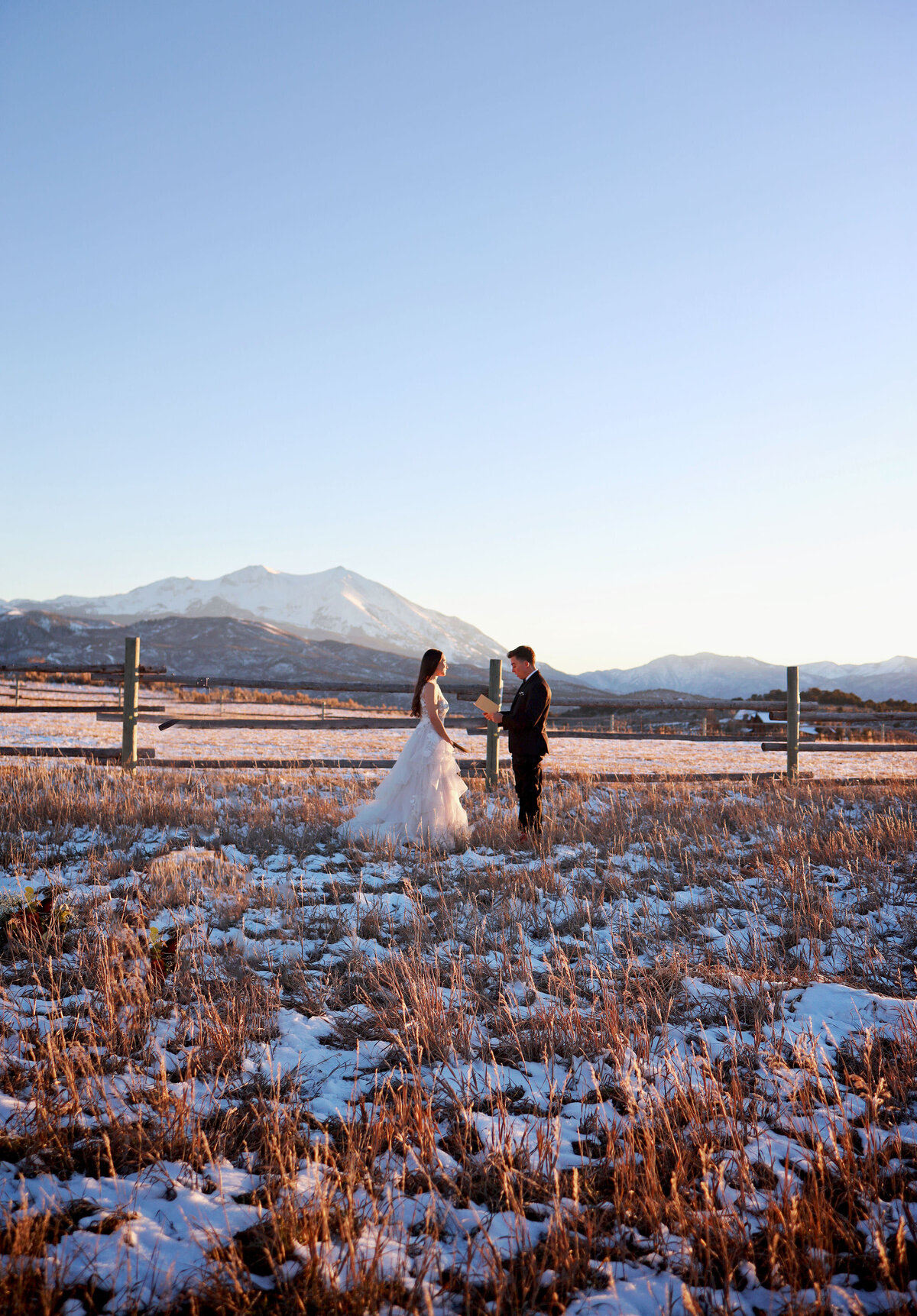 A bride and groom standing in front of a white snowy mountain backdrop, eloping.