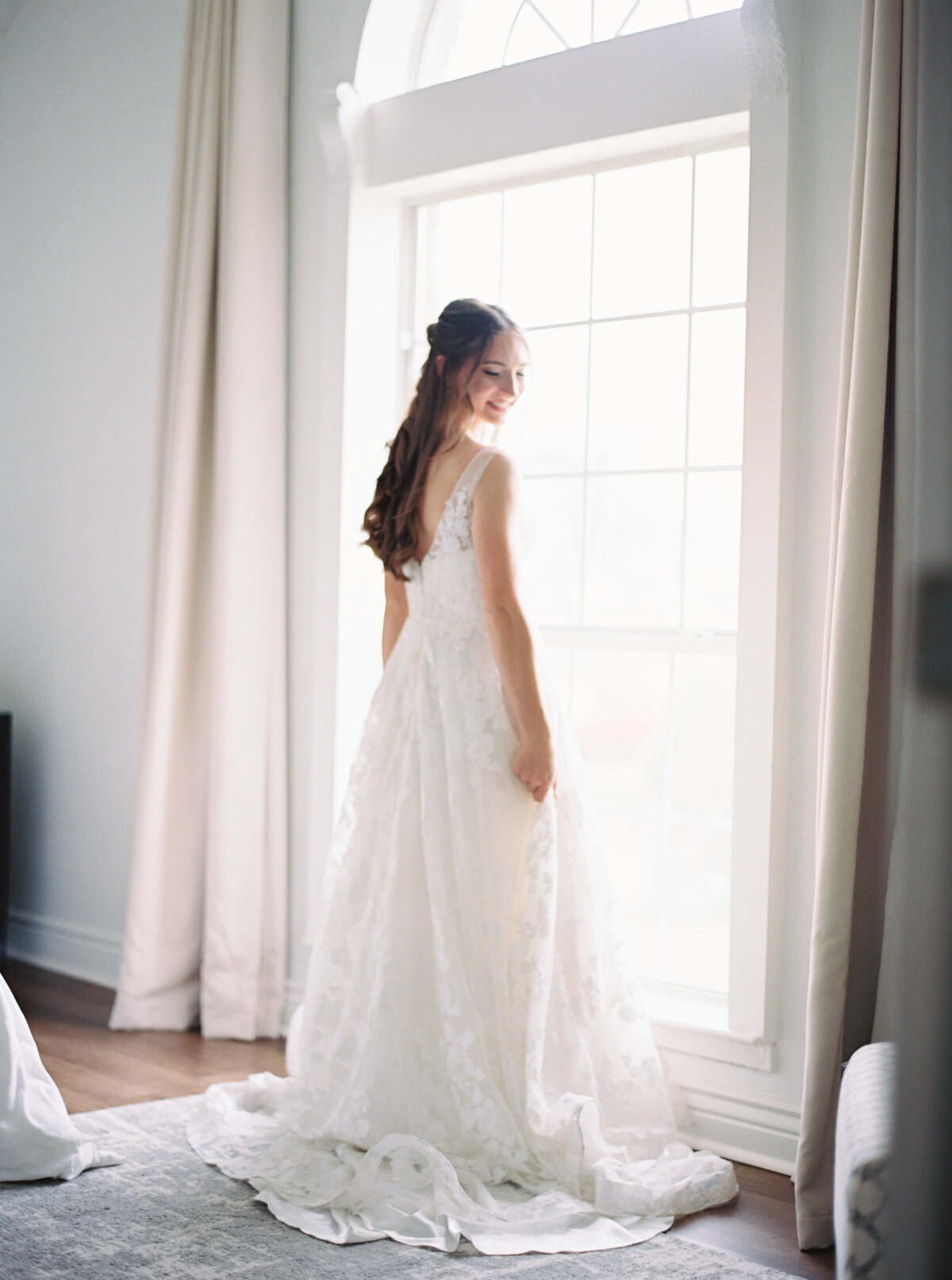 Bride standing in a window, showcasing her wedding dress in an elegant moment before the ceremony, captured by Morgan Alysse, Lafayette wedding photographer.