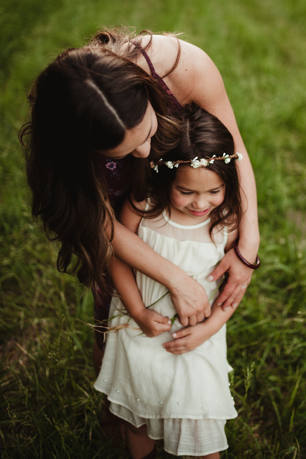 Mother hugs daughter wearing a flower crown and ivory dress from behind.