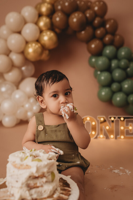 Cake smash milestone session with Atlanta, Georgia cake smash photographer. Milestone photography session with earthy tones, balloon garland and sweet baby boy eating cake for his first birthday.