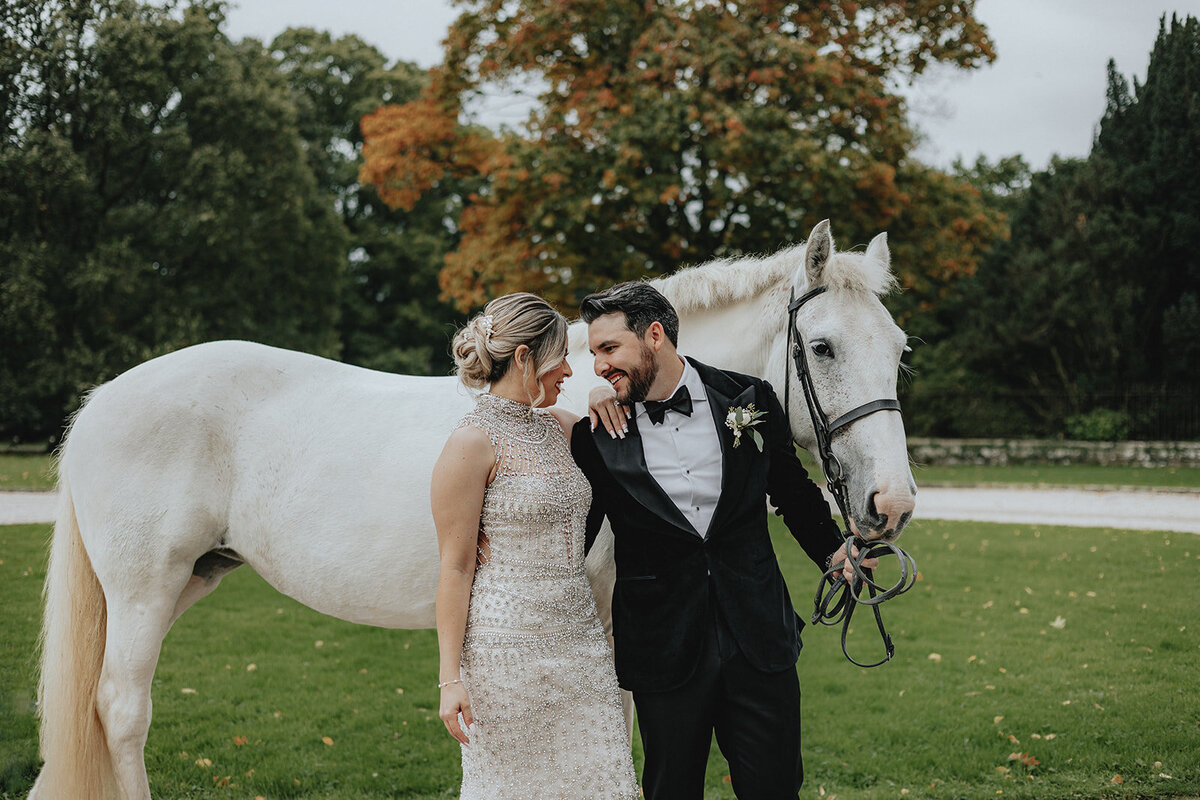 Bride looking at groom holding the reigns of a white horse