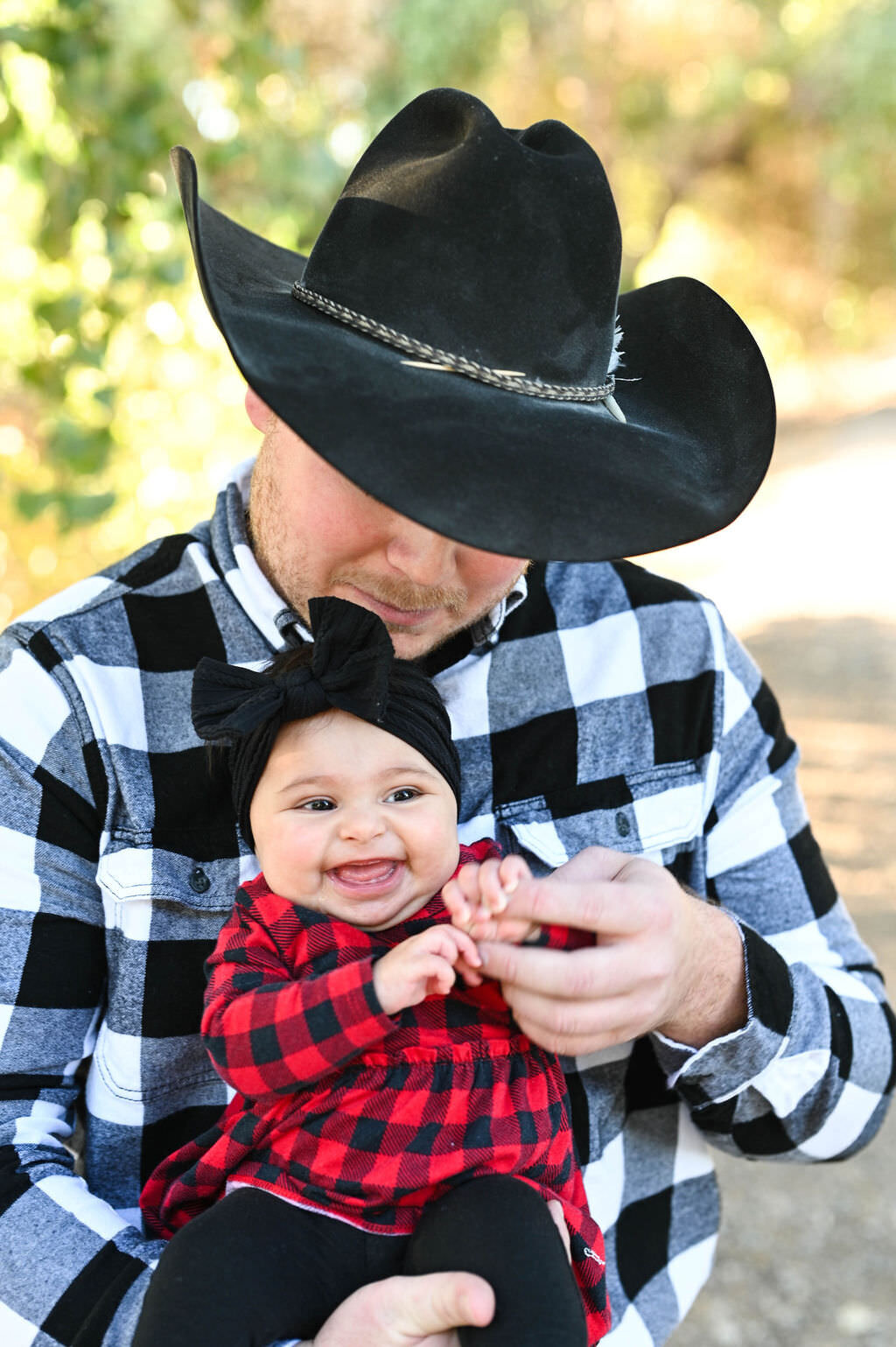 A dad in a cowboy hat holding a baby as she smiles.