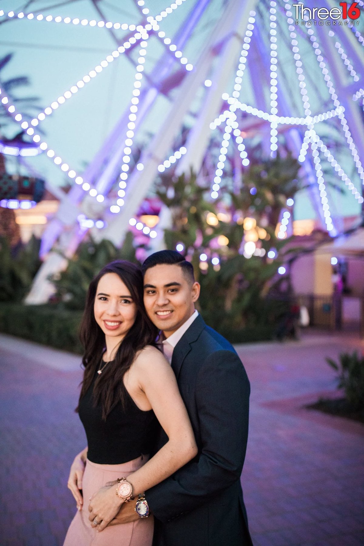 Groom to be embraces his Bride in front of the Ferris Wheel