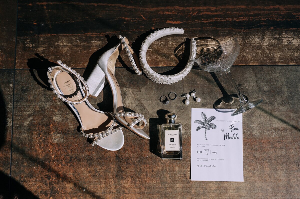 flat lay of brides white details on wedding day like harlo beaded shoes and a white beaded headband with jo malone perfume