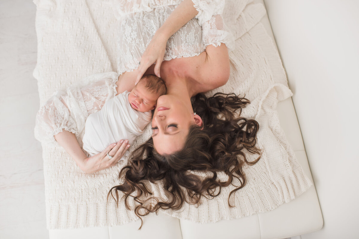 a shot from above with a mom and baby laying on a white blanket