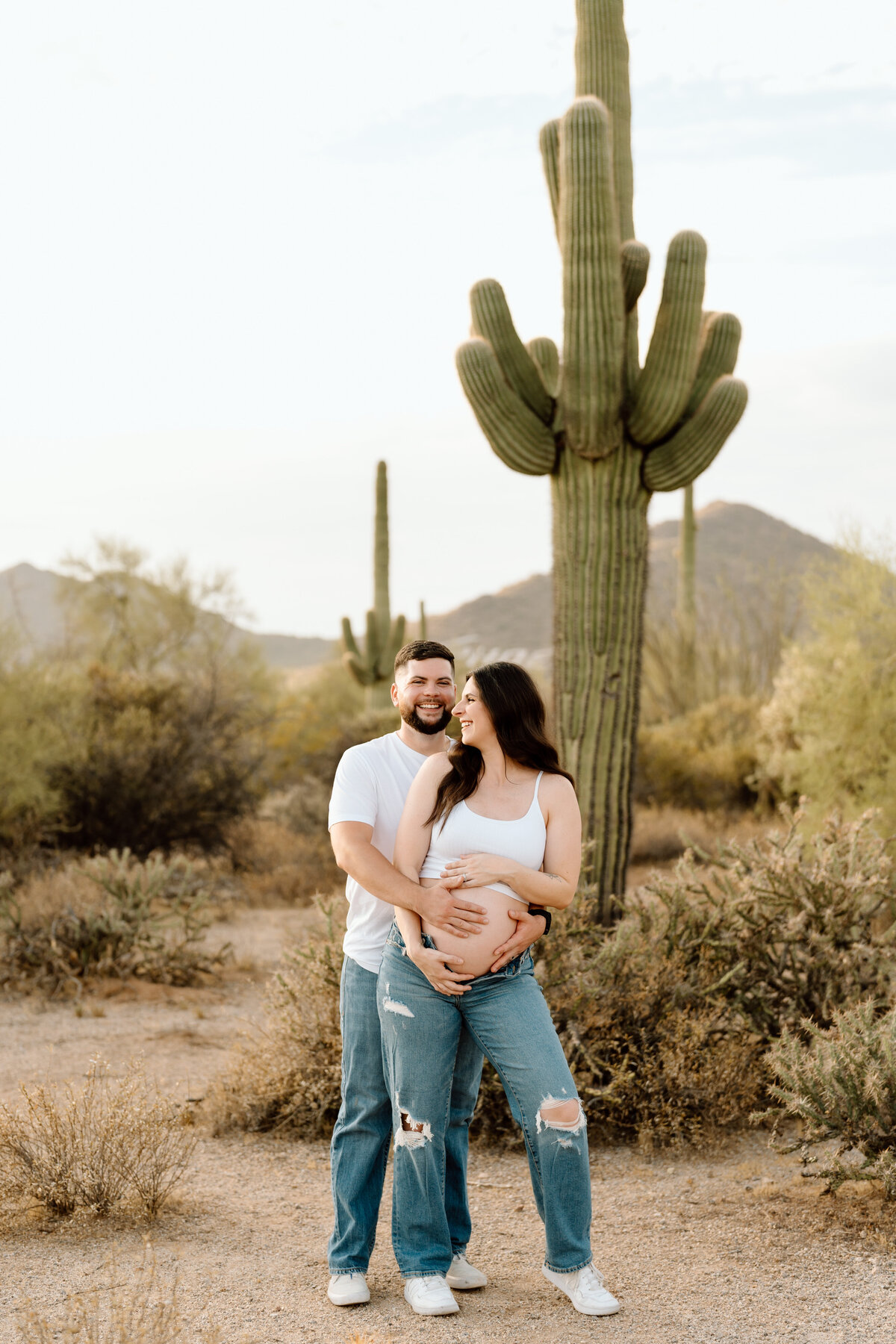 Man holding pregnant wife's stomach standing in front of a cactus