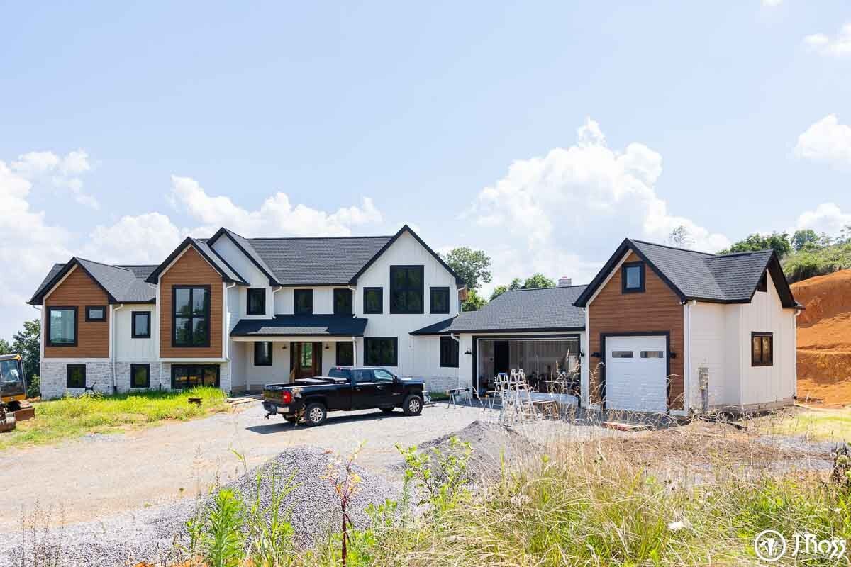 Full front view of a two-story modern farmhouse with contrasting white and natural wood-look siding, dark roofing, and black trim, showcasing professional home outside painting, Kingsport, Tennessee.