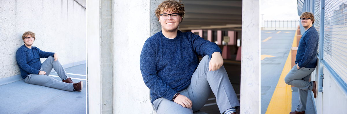 Caucasian senior boy wearing a blue sweater, gray dress, and brown casual shoes sitting against a brick wall and standing against a fence posing casually.