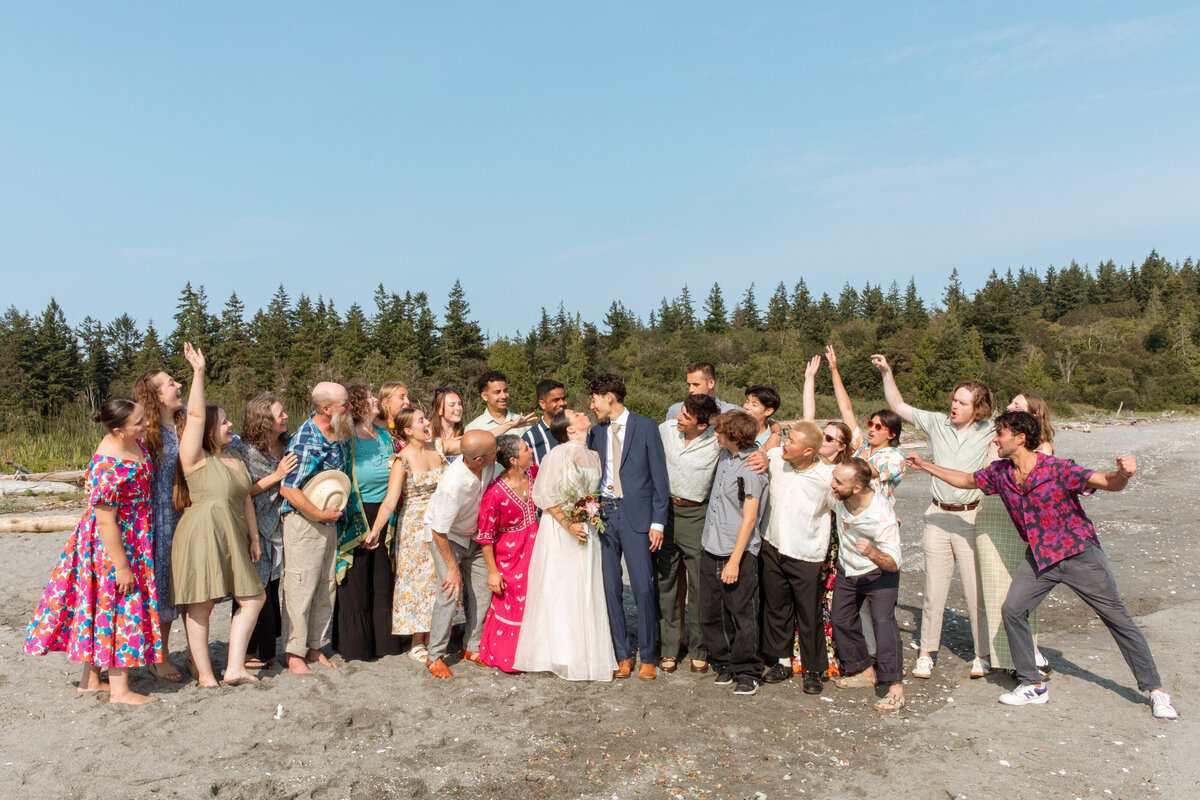 Family and friends surround the bride and groom on the beach on their wedding day