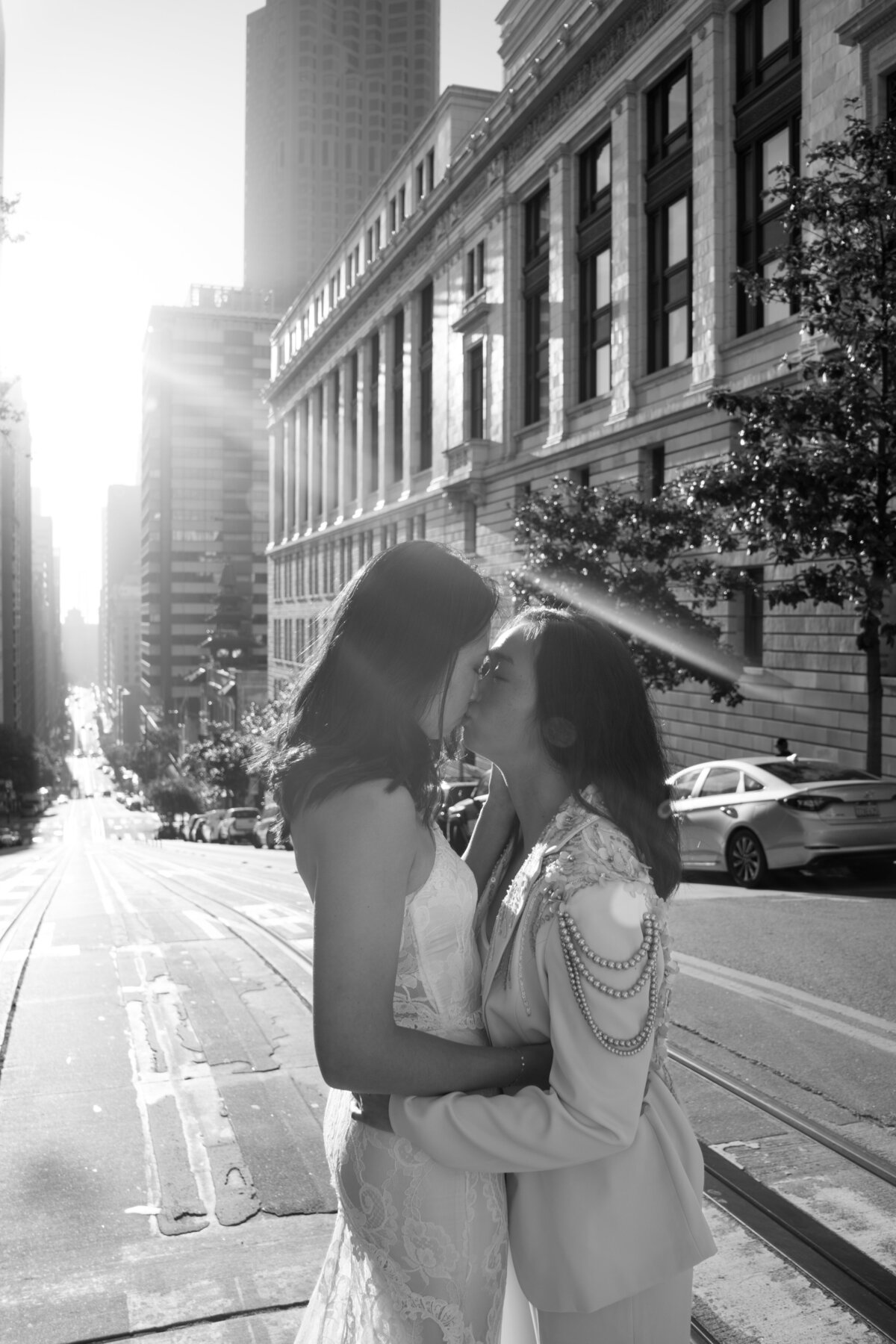 Black and white portrait of queer lesbian brides in San Francisco kissing at sunrise with a sun ray beaming behind them