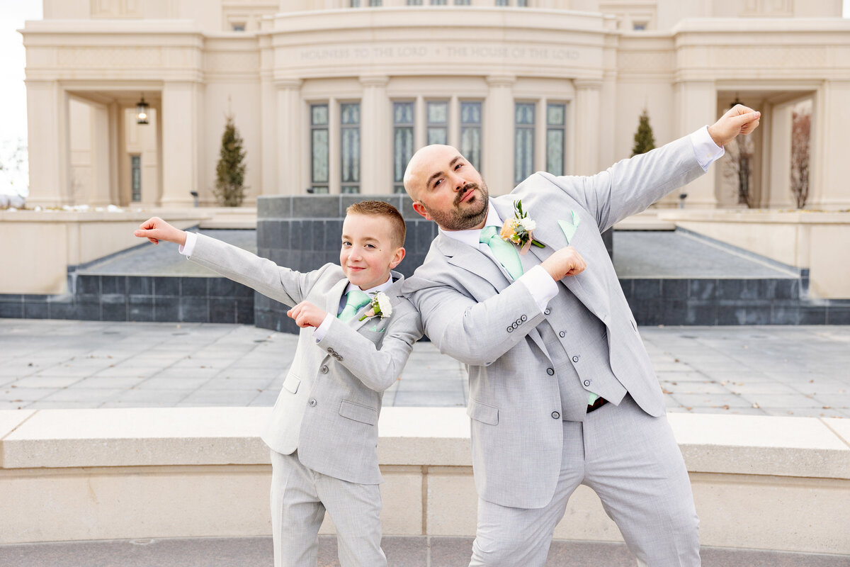 The groom and young boy strike a playful superhero pose in matching gray suits and mint green ties