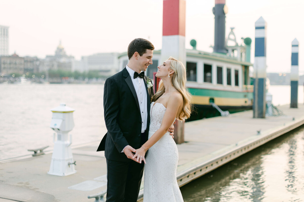 A bride and groom look at one another in front of a tug boat.
