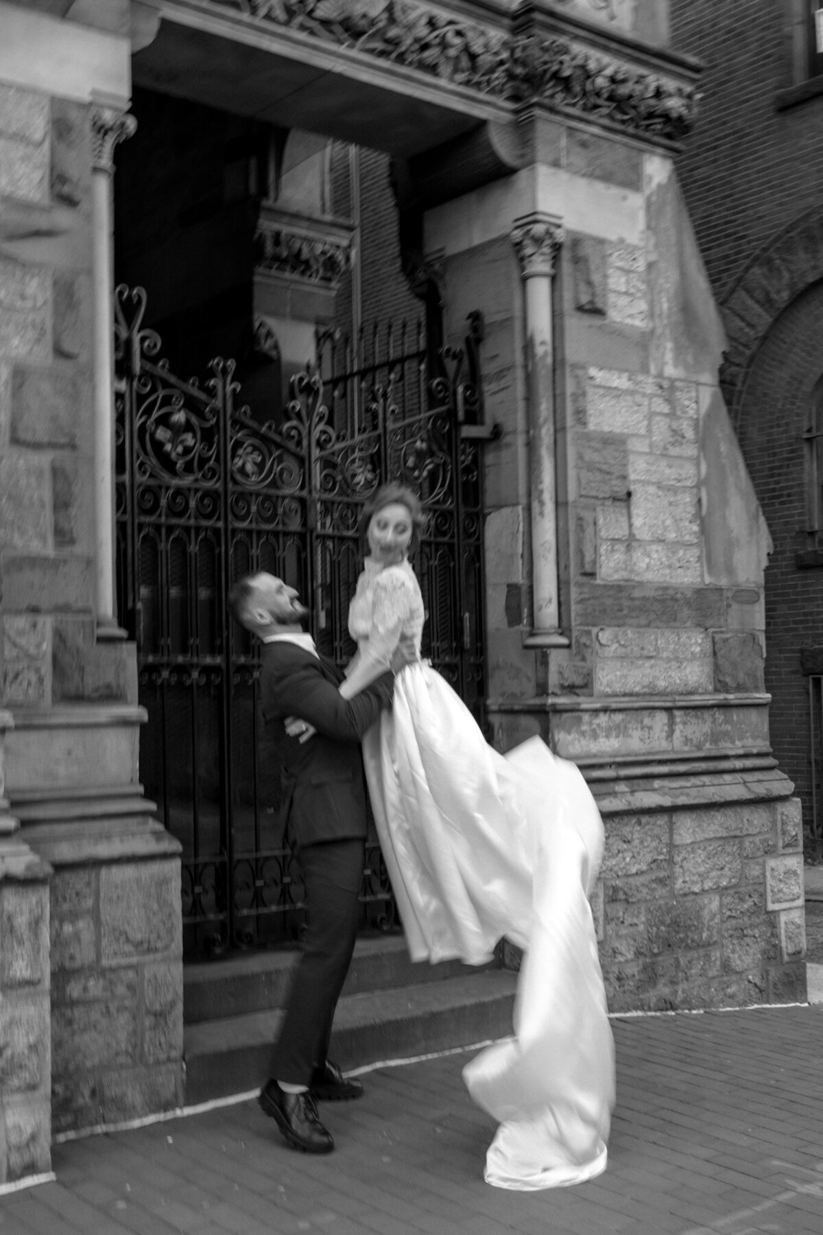 Groom sweeping his bride in his arms. A black-and-white, vintage photo depicting a dramatic, romantic gesture. Newly married couple in a black suit and white wedding dress.