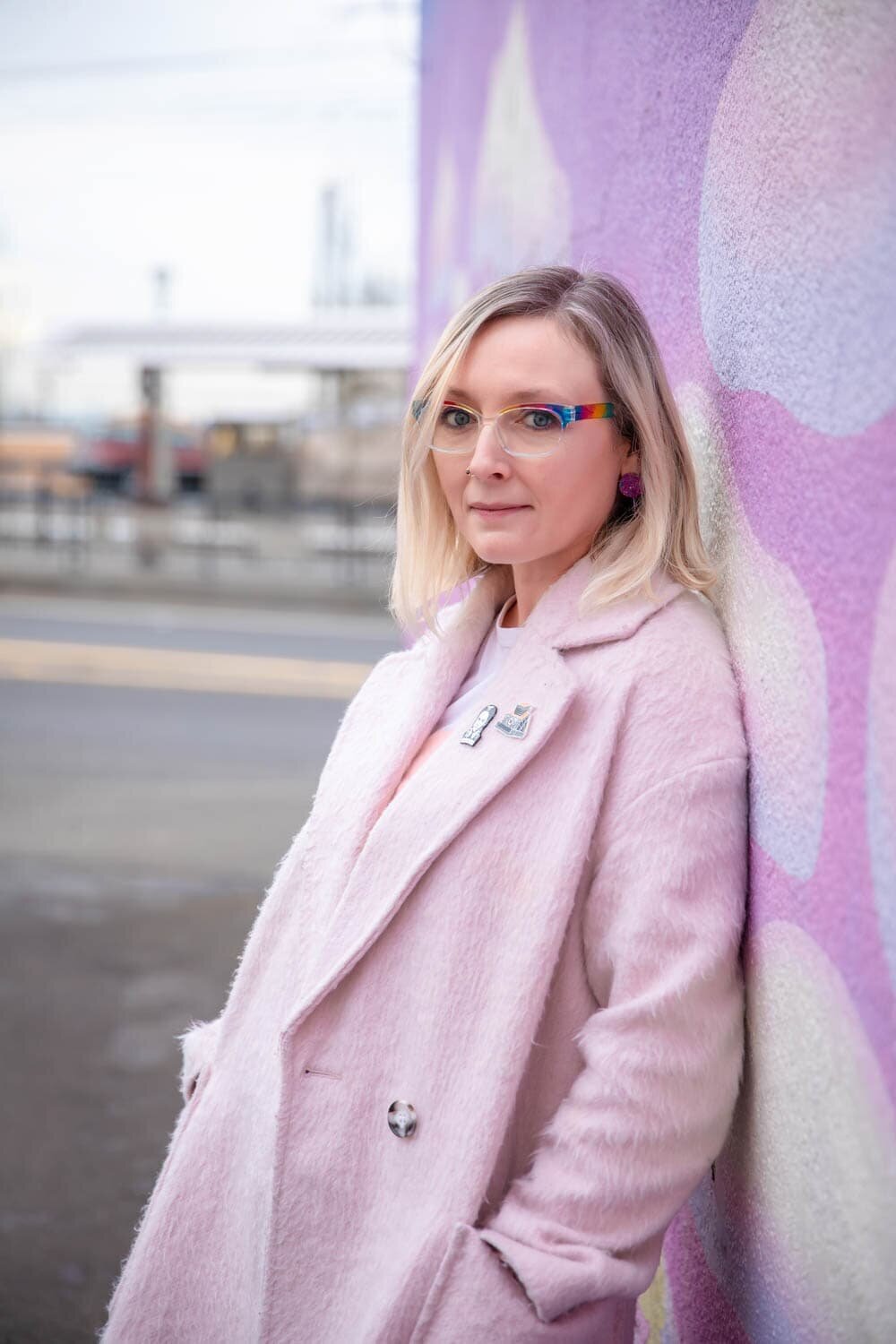 crystal genes photography wears a pink coat in front of a pink mural with clouds