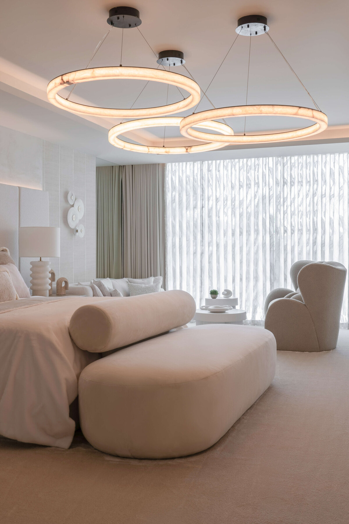 A large, contemporary light fixture composed of three circles emits a soft, warm light on the spacious primary bedroom.