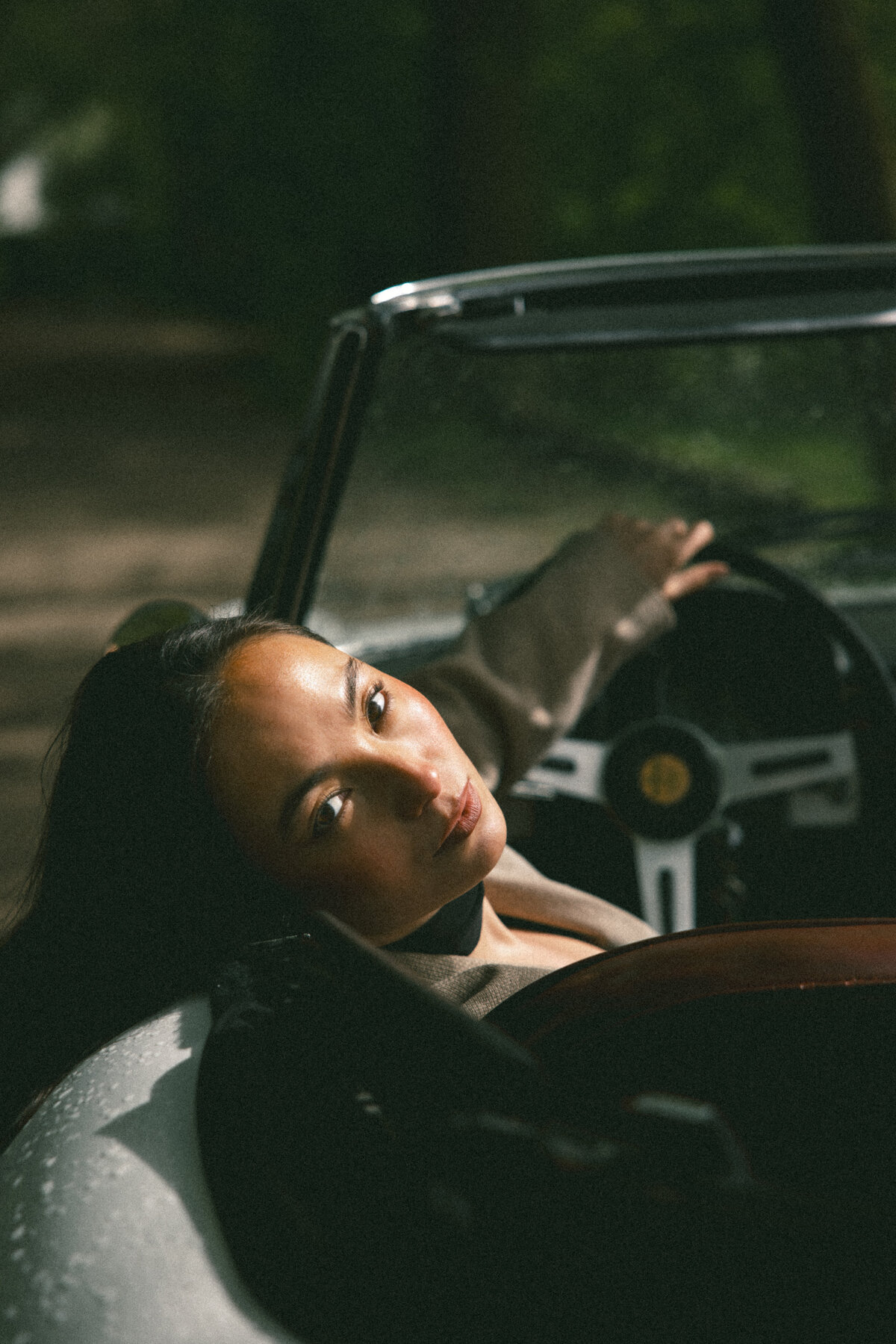 An evocative image showing the subject in a classic suit, standing beside her vintage car. The wide-angle view of the car and the road ahead symbolizes a journey, both literal and metaphorical, with the subject ready to embark, photographed by Bo Eppink.