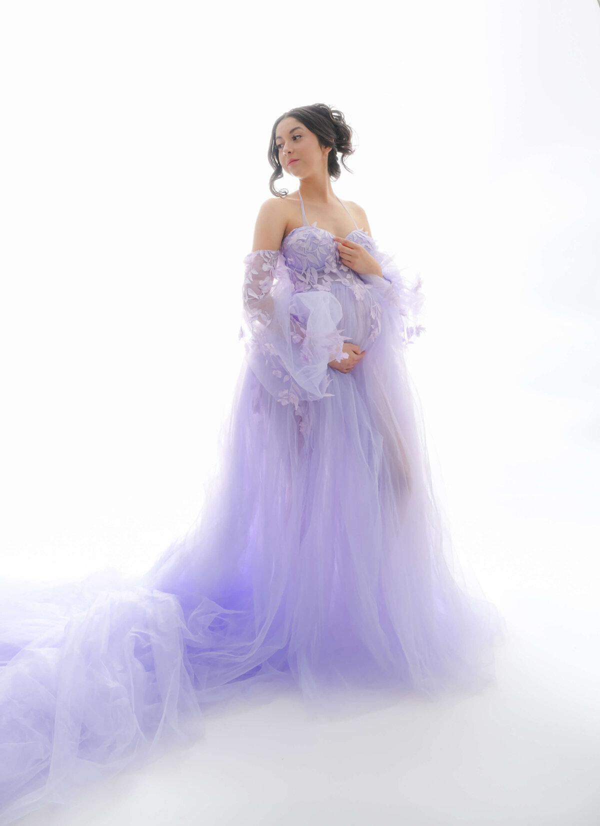 Maternity photo session with back lighting.  Expectant mother is looking over her shoulder and wearing a floor length, lavender, off the should dress.Image by E. Benecki Photography