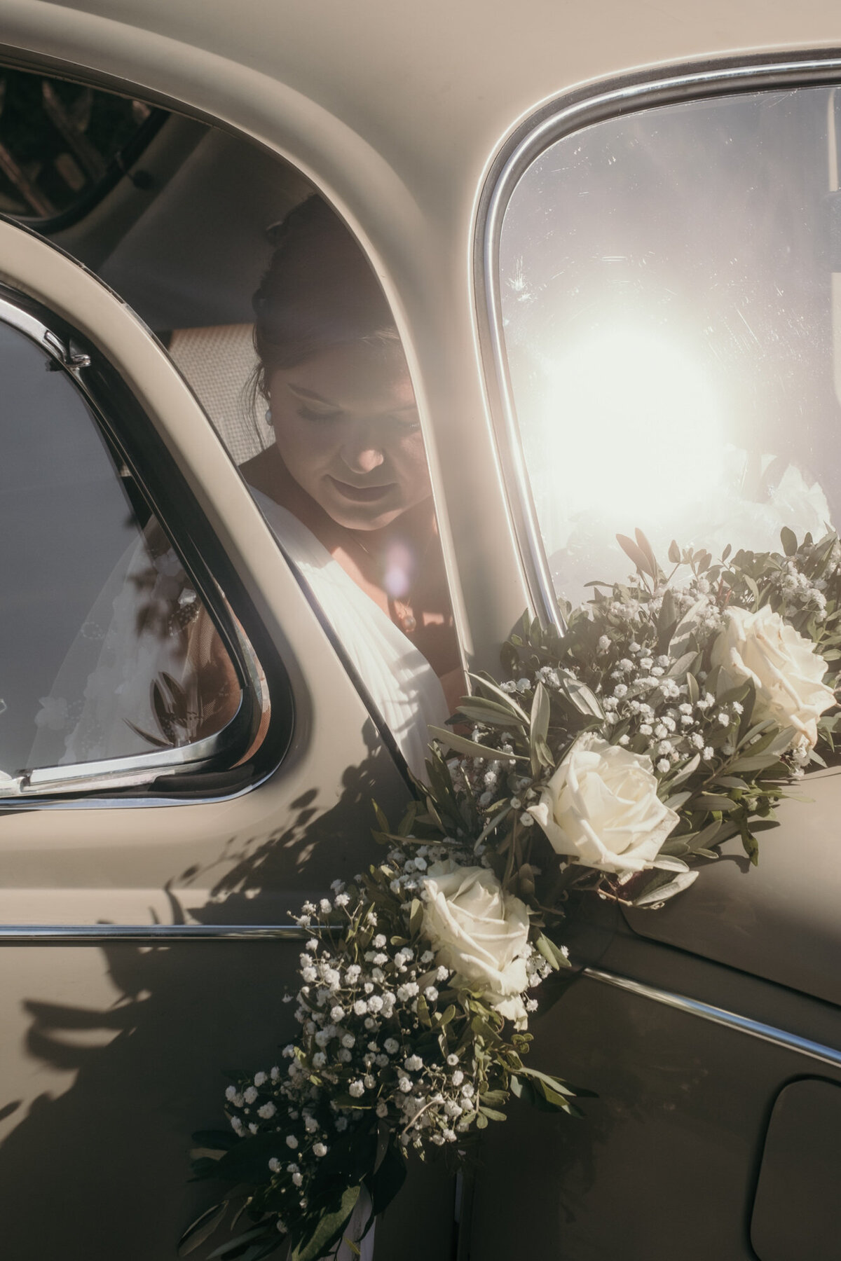 Dieser Ausschnitt zeigt, wie die Braut gerade in das mit Blumen geschmückte Hochzeitsauto eingestiegen ist.