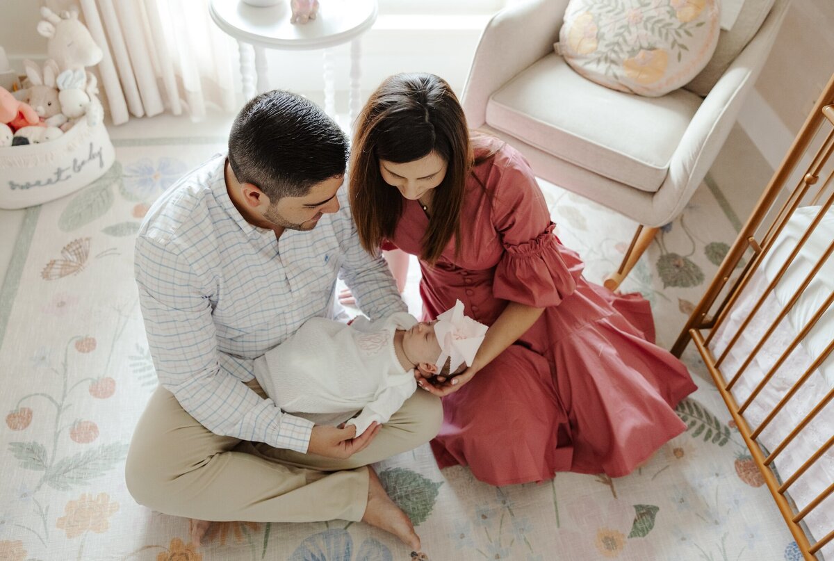 couple sits on the floor of their nursery with their newborn