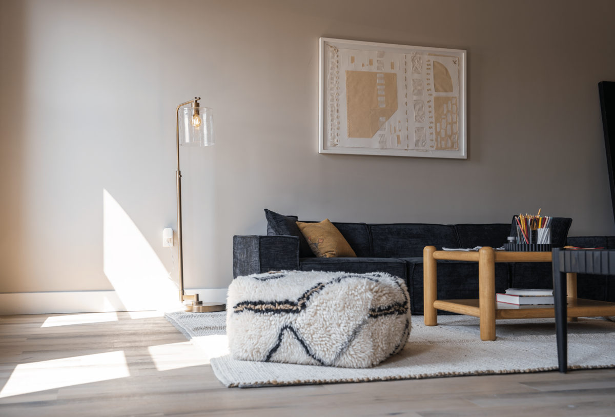 Welcome lounge with large artwork over a comfy couch. A wooden sofa table with art supplies sits atop a large, cozy area rug next to a plush ottoman.