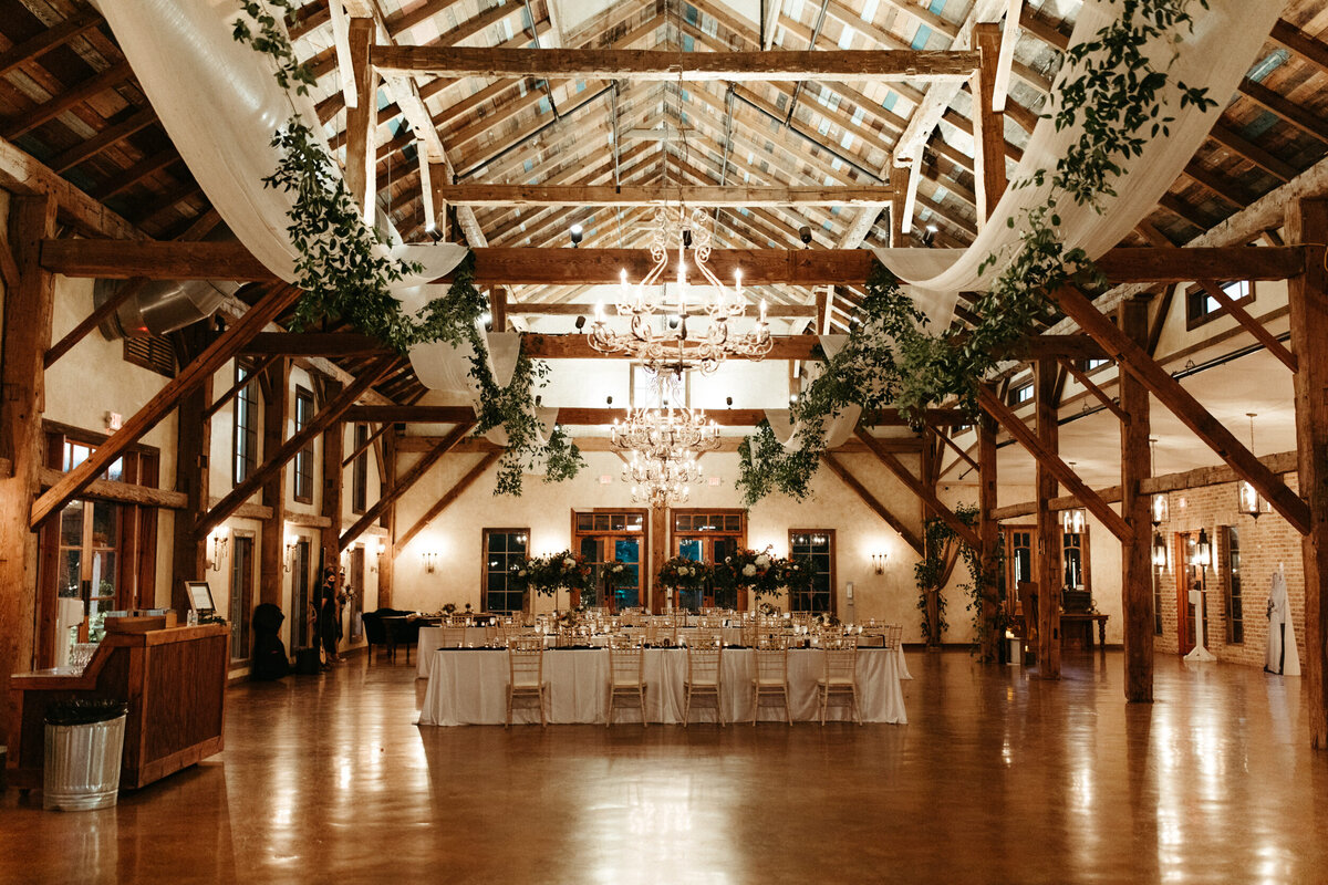 Elaborate wedding reception hall decorations with greenery and drapery hanging around chandeliers