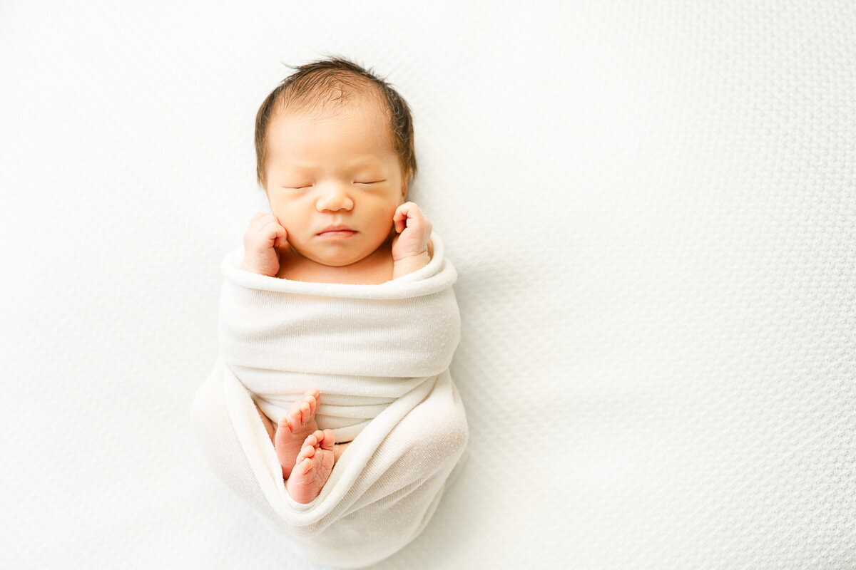 an infant child lays asleep on a white surface for her infant photography session in Austin, TX.