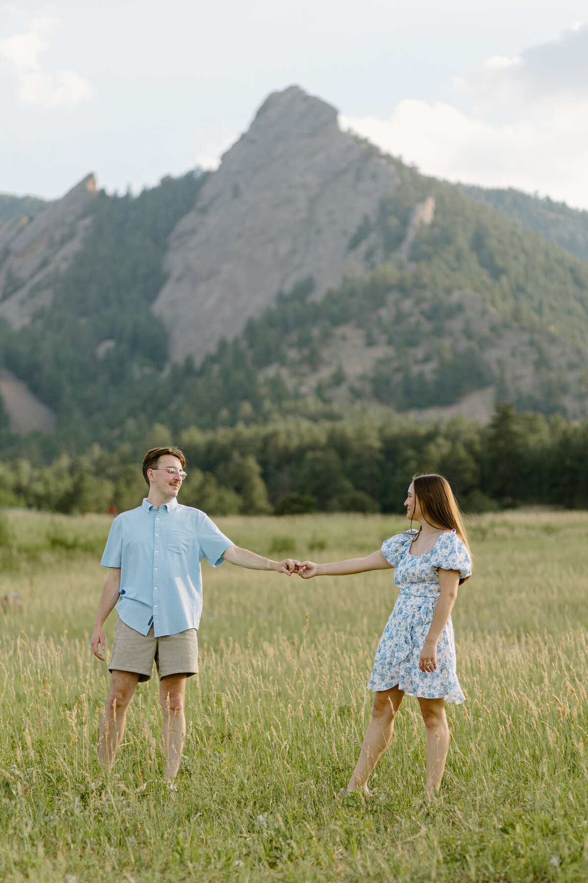 An engaged couple holding hands in front of the iconic Flatirons at Chautauqua Trailhead in Boulder, Colorado, during their engagement session.