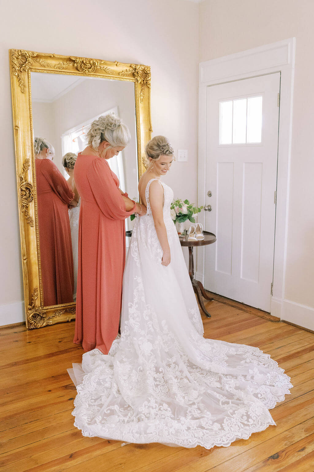 Bride's mom wearing coral dress and zipping bride into wedding gown