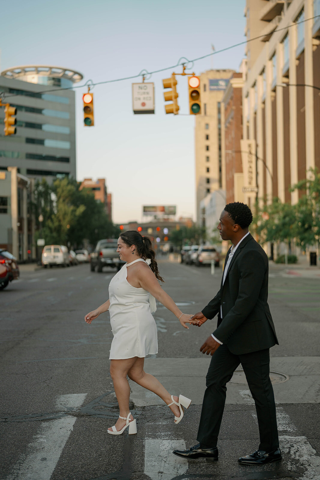 Fun downtown Kalamazoo engagement photo of couple crossing the street hand in hand.